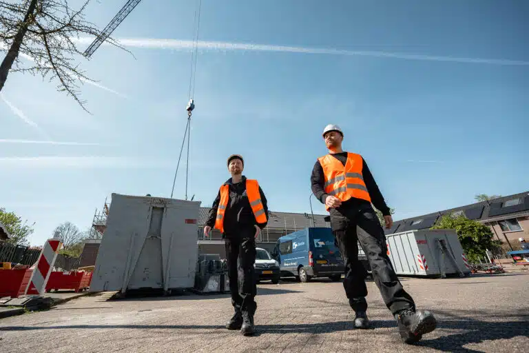 Twee medewerkers van Verdo Werkt lopen in oranje hesjes over het terrein